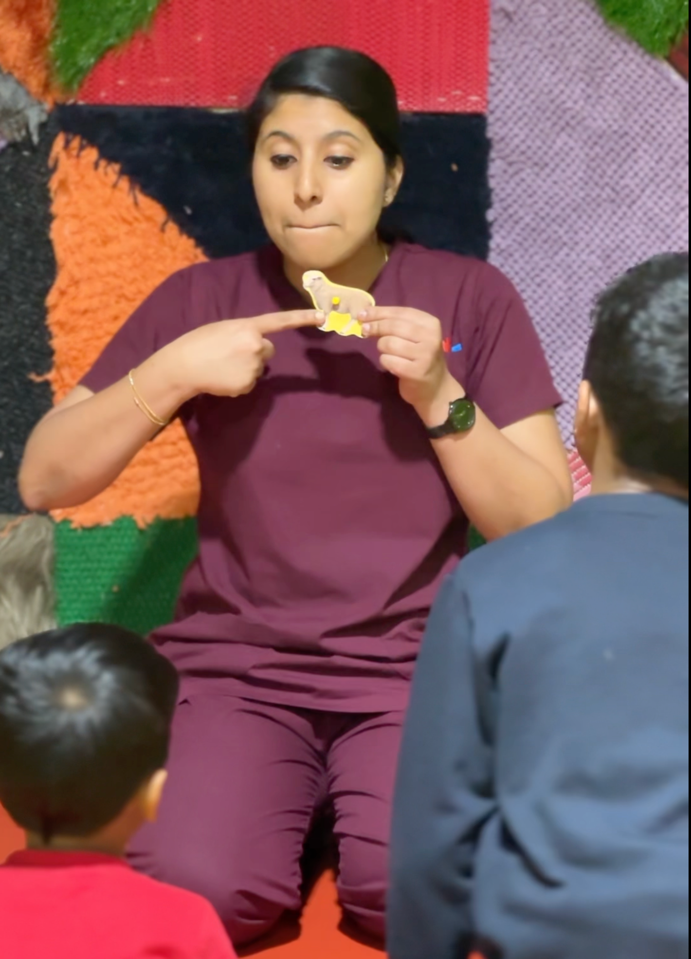 A speech therapist using a toy and expressive gestures to teach a group of children during a therapy session.